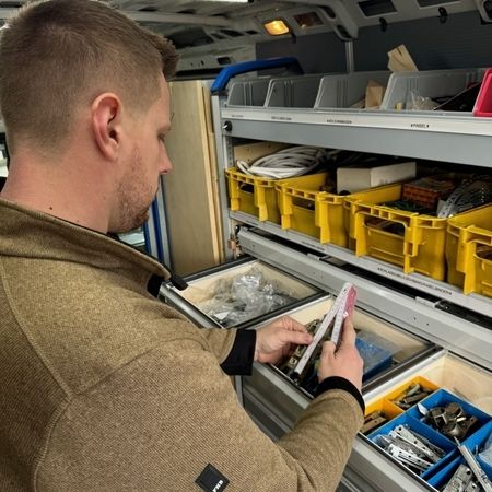 Ein Tischler steht vor einem Materialschrank und hat einen Zollstock in der Hand