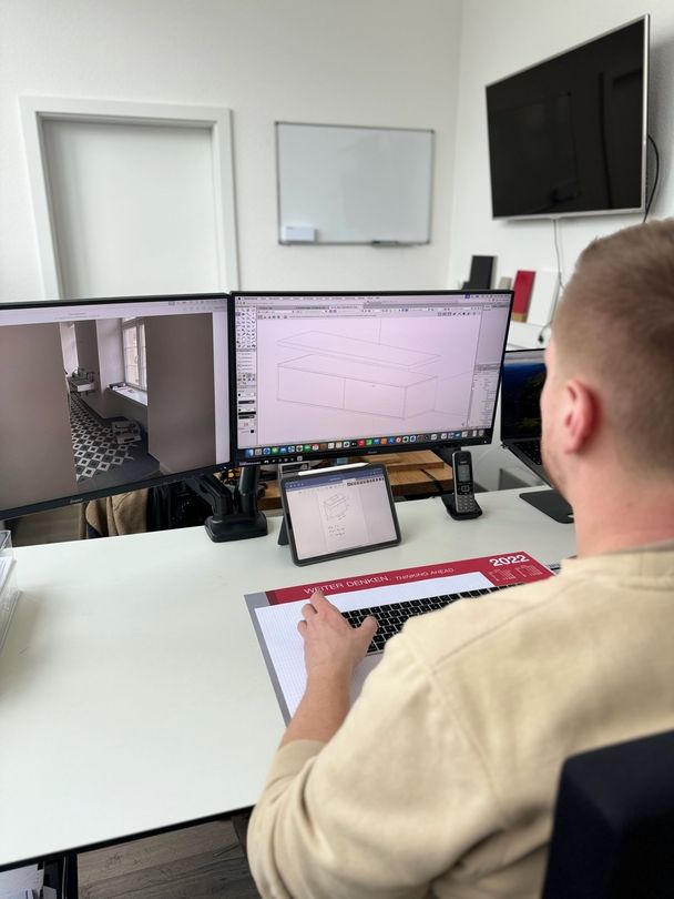 Ein Tischler sitzt vor einem Bildschirm und bearbeitet das Design eines Möbelstücks